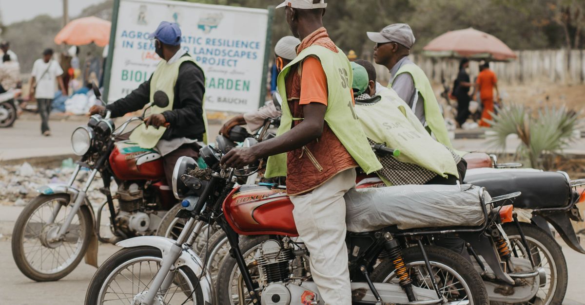 Group Of Motorbike Riders Wearing Vests In A Bustling African City Street Scene.