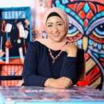 Cheerful Woman In Hijab Posing Indoors With A Colorful Graffiti Owl Artwork Behind Her.