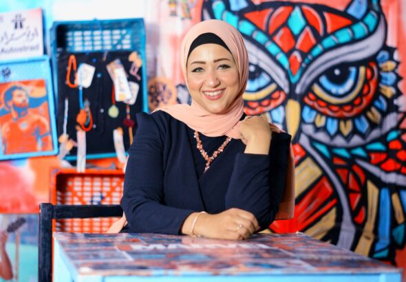 Cheerful Woman In Hijab Posing Indoors With A Colorful Graffiti Owl Artwork Behind Her.