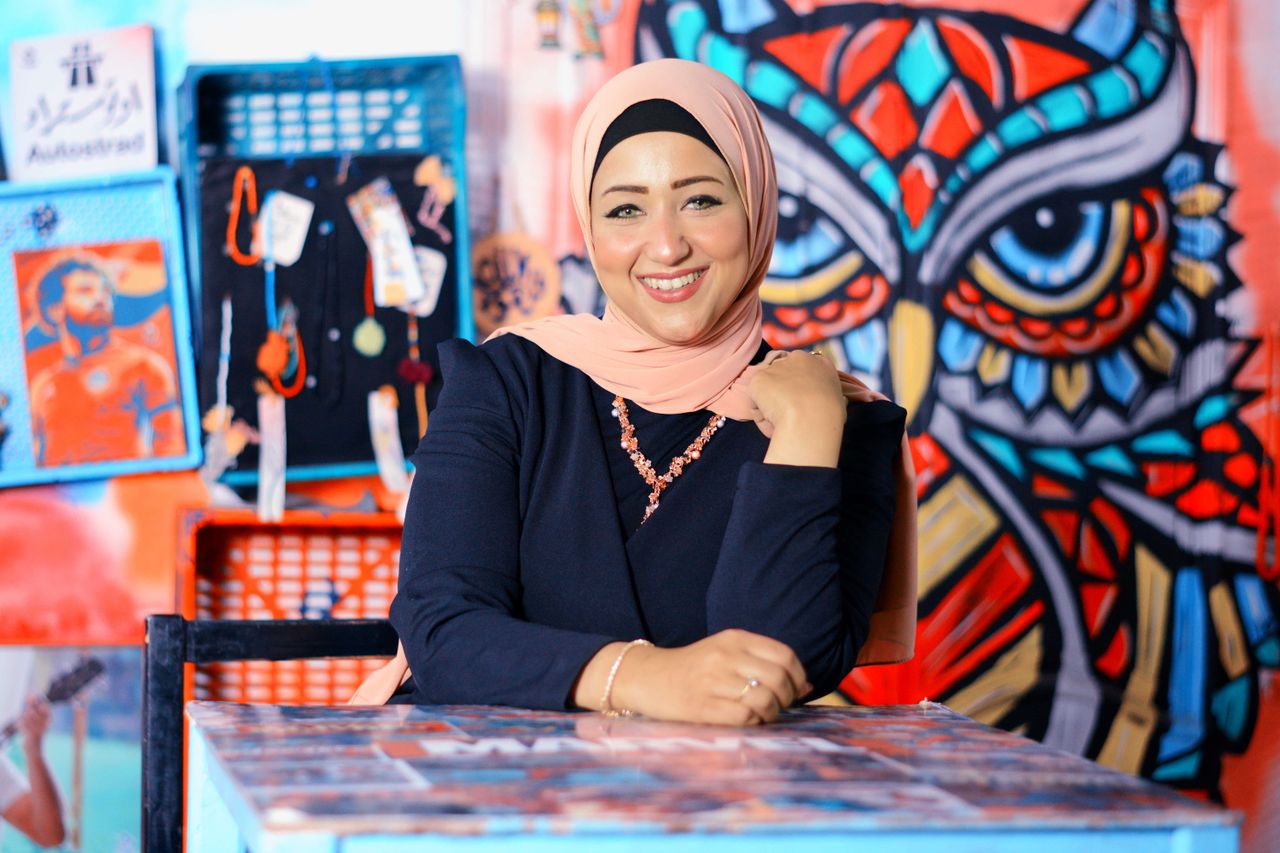 Cheerful Woman In Hijab Posing Indoors With A Colorful Graffiti Owl Artwork Behind Her.