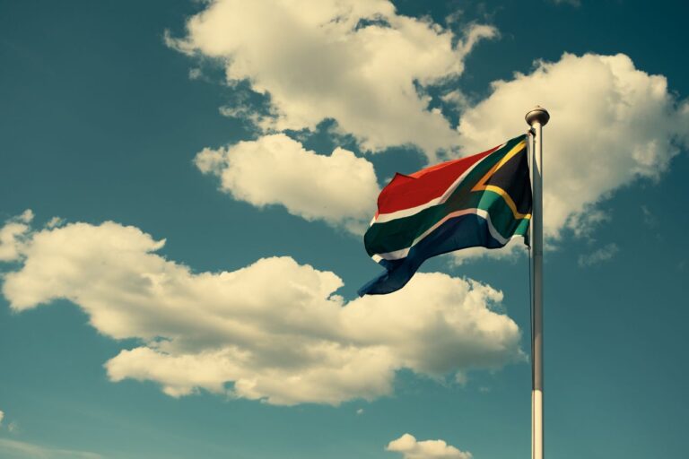 South African Flag Waving Against A Bright Blue Sky With Clouds.